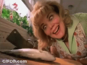 A Woman Is Looking At A Fish On A Cutting Board And Smiling . GIF
