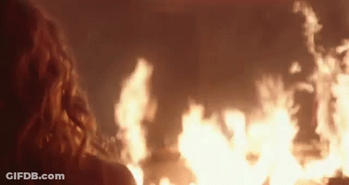 A Woman Is Looking At A Large Fire In The Dark . GIF