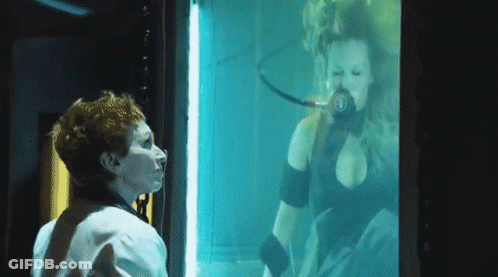 A Woman Is Looking At A Woman In A Tank With The Letter B On Her Chest GIF