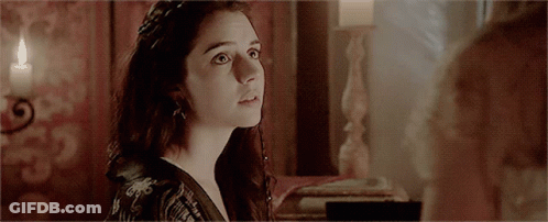 A Woman Is Looking At Another Woman In A Room With A Candle In The Background GIF