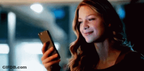 A Woman Is Looking At Her Cell Phone In The Dark . GIF