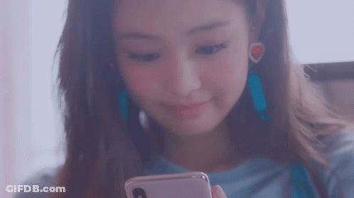 A Woman Is Looking At Her Phone And Smiling While Wearing Earrings . GIF
