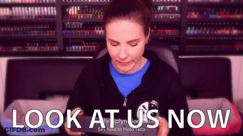 A Woman Is Looking At Her Phone With The Words Look At Us Now Behind Her GIF