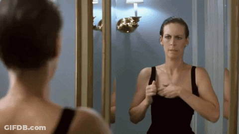 A Woman Is Looking At Her Reflection In A Mirror . GIF