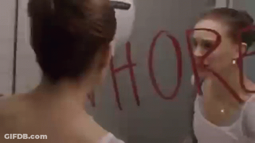A Woman Is Looking At Her Reflection In A Mirror And The Word Whore Is Written On The Mirror . GIF