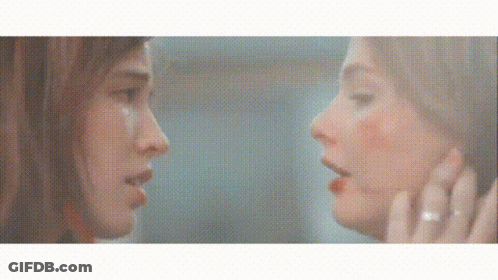 A Woman Is Looking At Her Reflection In A Mirror And Touching Her Face . GIF