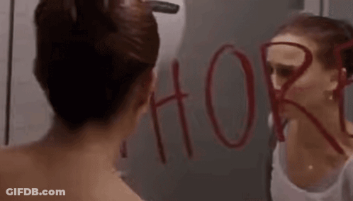 A Woman Is Looking At Herself In A Bathroom Mirror With The Word Whore Written On It . GIF