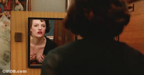 A Woman Is Looking At Herself In A Mirror GIF