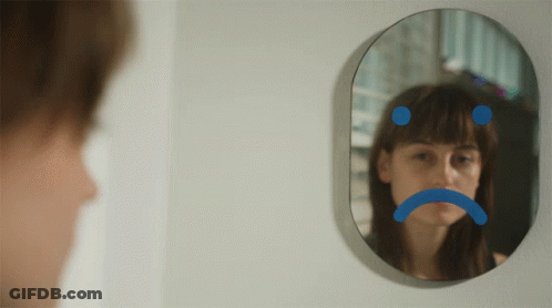 A Woman Is Looking At Herself In A Mirror With A Sad Face Drawn On It GIF