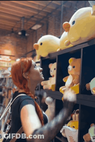 A Woman Is Looking At Stuffed Animals On A Shelf GIF