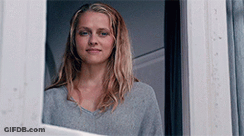 A Woman Is Looking Out Of A Window And Smiling . GIF