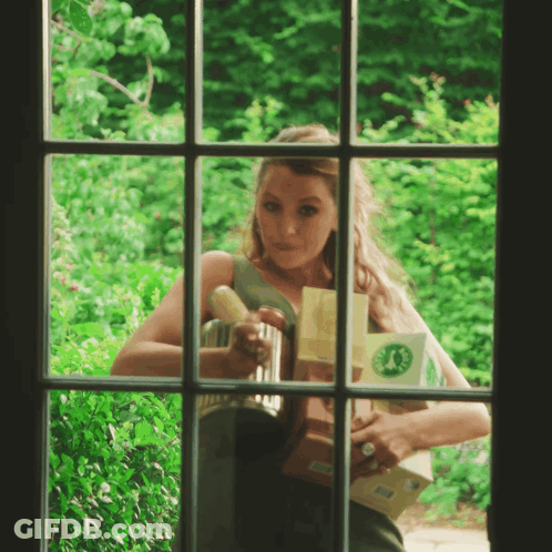 A Woman Is Looking Out Of A Window Holding A Box With A Green Circle On It GIF