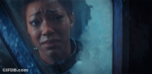 A Woman Is Looking Out Of A Window With A Sad Look On Her Face GIF