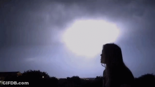 A Woman Is Looking Up At A Lightning Storm In The Sky . GIF