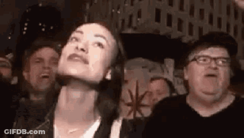 A Woman Is Looking Up At Something In A Crowd Of People At A Concert . GIF