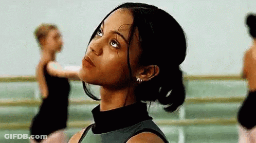 A Woman Is Looking Up At The Sky In A Dance Studio While Other Dancers Are Dancing In The Background . GIF