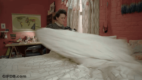 A Woman Is Making A Bed With A Map Of The World Hanging On The Wall Behind Her GIF
