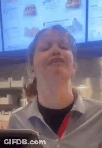 A Woman Is Making A Funny Face In Front Of A Menu In A Fast Food Restaurant . GIF