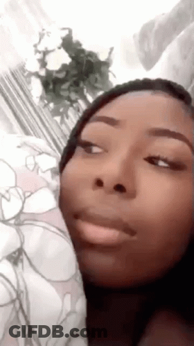 A Woman Is Making A Funny Face While Laying On A Bed With Flowers In The Background . GIF