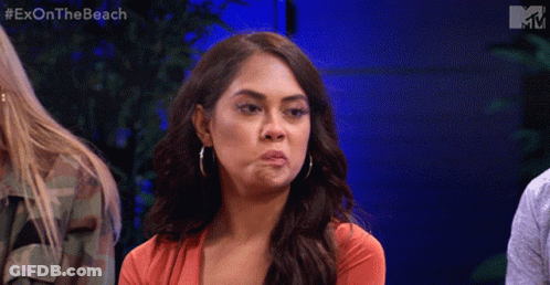 A Woman Is Making A Funny Face While Sitting In Front Of A Blue Wall With The Words Exon The Beach On It GIF