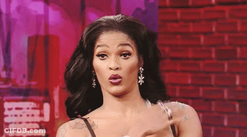 A Woman Is Making A Funny Face While Standing In Front Of A Red Brick Wall . GIF