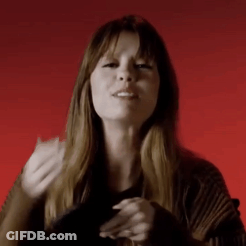 A Woman Is Making A Gesture With Her Hands In Front Of A Red Background While Wearing A Black Sweater . GIF