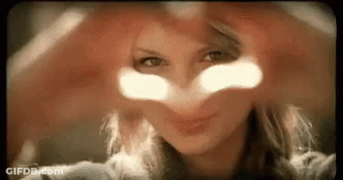 A Woman Is Making A Heart With Her Hands In Front Of Her Face . GIF