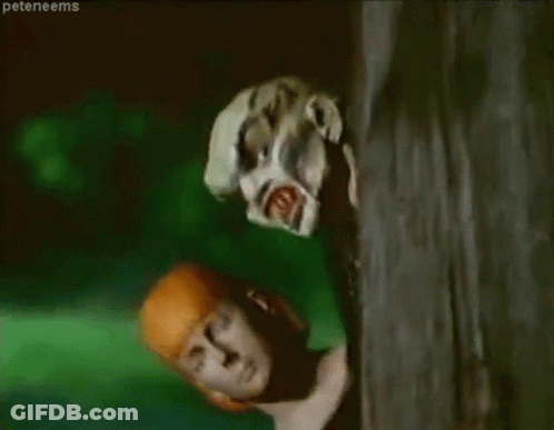 A Woman Is Peeking Out From Behind A Tree While A Zombie Is Looking At Her . GIF