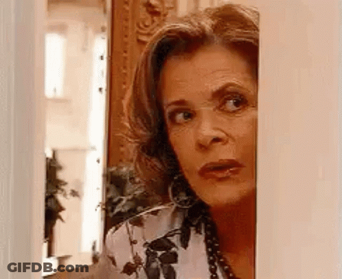 A Woman Is Peeking Out From Behind A Wall And Looking At The Camera . GIF