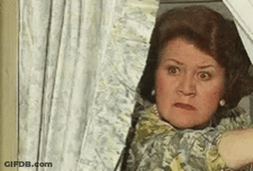A Woman Is Peeking Out Of A Window With A Shocked Look On Her Face . GIF