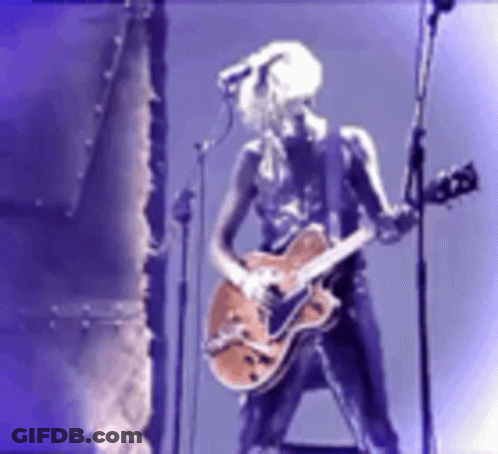 A Woman Is Playing A Guitar And Singing Into A Microphone GIF