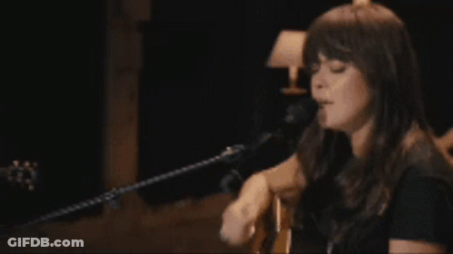 A Woman Is Playing A Guitar And Singing Into A Microphone GIF