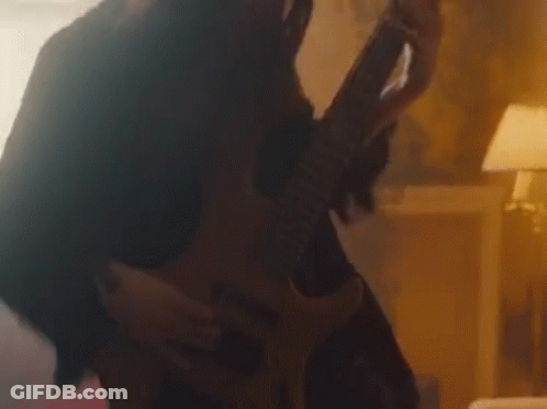 A Woman Is Playing A Guitar In A Dark Room While A Man Is Holding Her . GIF