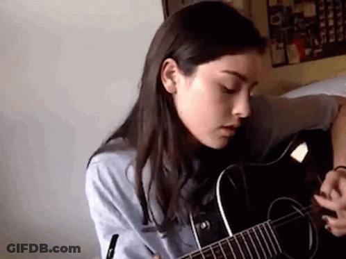 A Woman Is Playing A Guitar In A Room . GIF