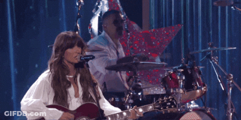 A Woman Is Playing A Guitar While A Man Plays Drums GIF