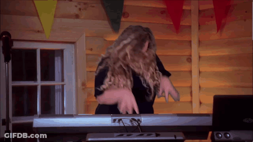 A Woman Is Playing A Keyboard In Front Of A Log Wall GIF