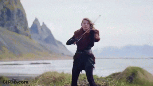 A Woman Is Playing A Violin In Front Of A Mountain And A Lake . GIF