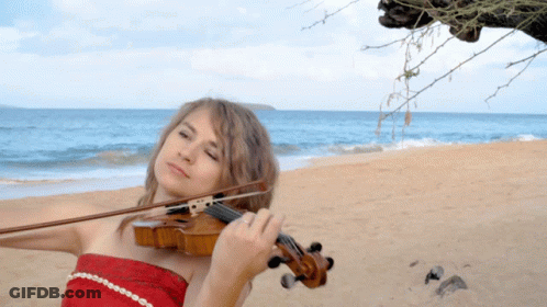 A Woman Is Playing A Violin On The Beach With The Ocean In The Background GIF