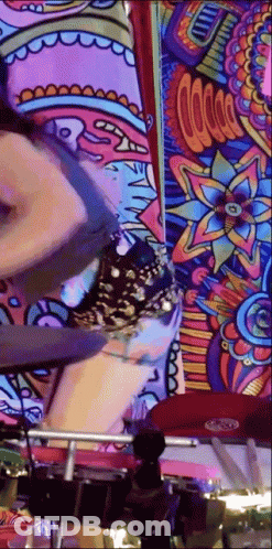 A Woman Is Playing Drums In Front Of A Colorful Wall Mural . GIF
