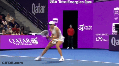 A Woman Is Playing Tennis In Front Of A Qatar Advertisement GIF