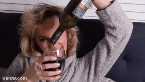 A Woman Is Pouring A Bottle Of Wine Into A Glass While Laying On A Couch . GIF