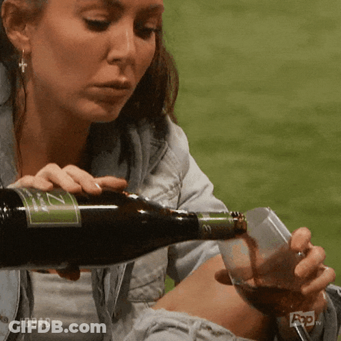 A Woman Is Pouring A Glass Of Wine From A Bottle With A Label That Says Z On It GIF