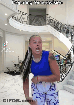 A Woman Is Preparing For Eurovision In Front Of A Spiral Staircase GIF