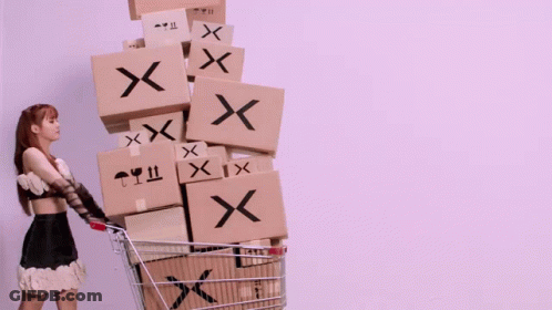 A Woman Is Pushing A Shopping Cart Filled With Boxes With X On Them GIF