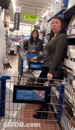 A Woman Is Pushing A Shopping Cart In A Walmart Aisle GIF