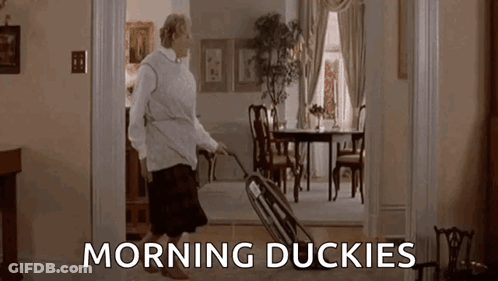 A Woman Is Pushing A Wheelbarrow Through A Living Room With The Words `` Morning Duckies '' Written On The Floor . GIF