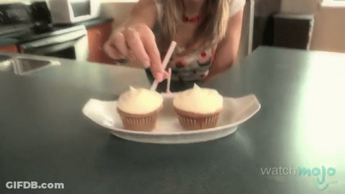 A Woman Is Putting Frosting On Two Cupcakes That Are On A Paper Plate GIF
