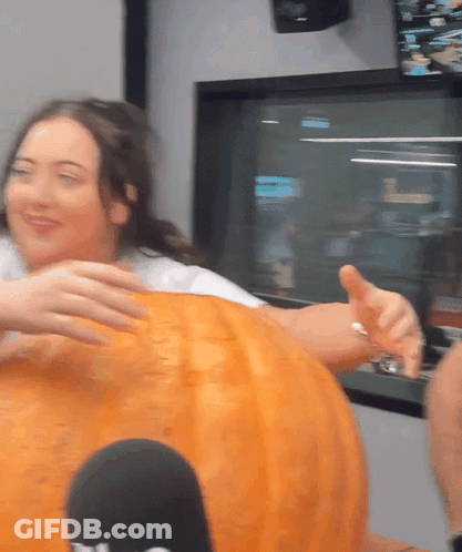 A Woman Is Putting Her Hand On A Pumpkin That Says ' T.v. ' On It GIF