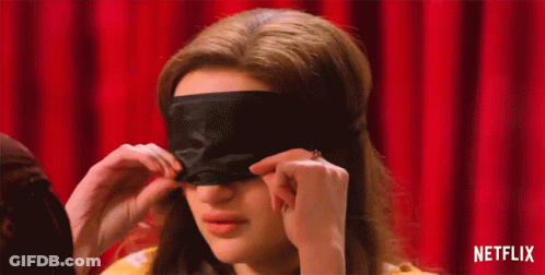 A Woman Is Putting On A Black Eye Mask On Her Face . GIF