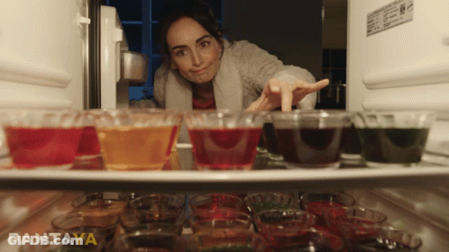 A Woman Is Reaching Into A Refrigerator Filled With Shot Glasses And Jelly GIF